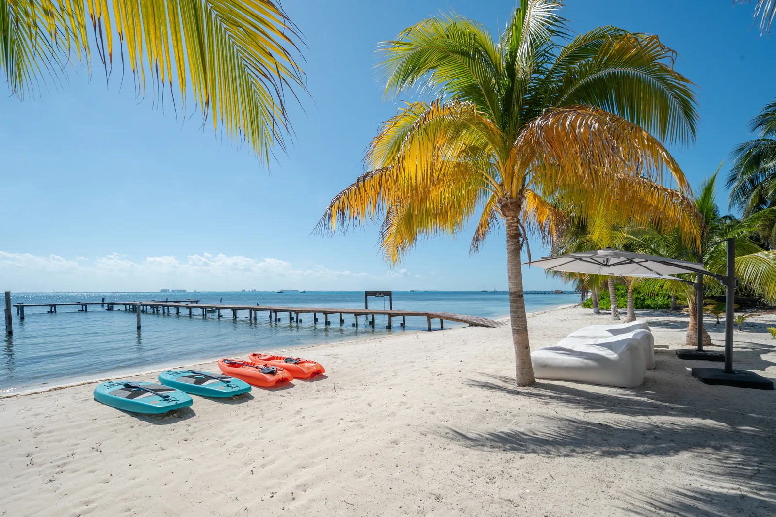 Kayaks and paddleboards on the white-sand beach in front of the residences, the dock beyond