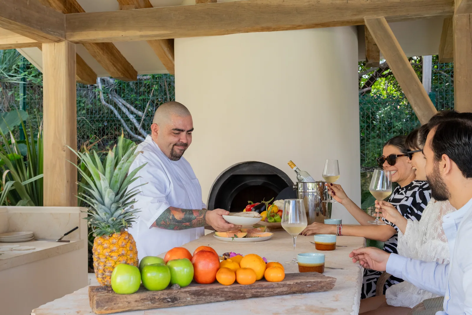 The chef serving guests at the wood-fired oven on the terrace, a fruit platter on the counter