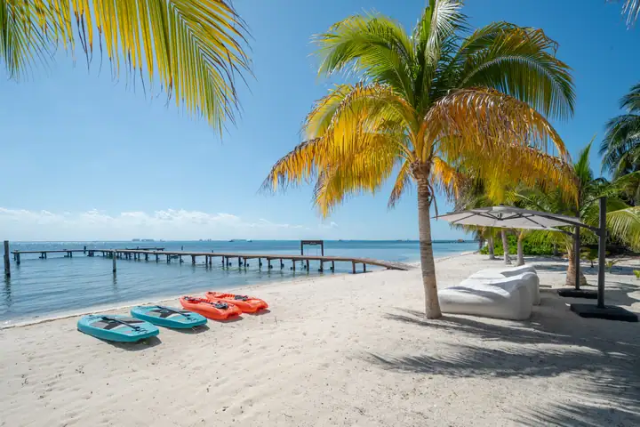 Kayaks and paddleboards on the white-sand beach in front of the residences, the dock beyond