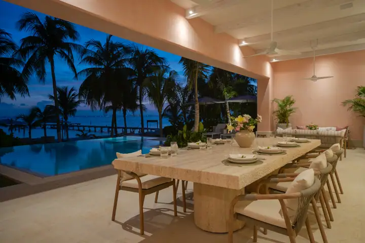 The terrace dining table at Casa Coral at dusk, the lit pool and the sea beyond