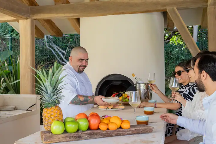 The chef serving guests at the wood-fired oven on the terrace, a fruit platter on the counter